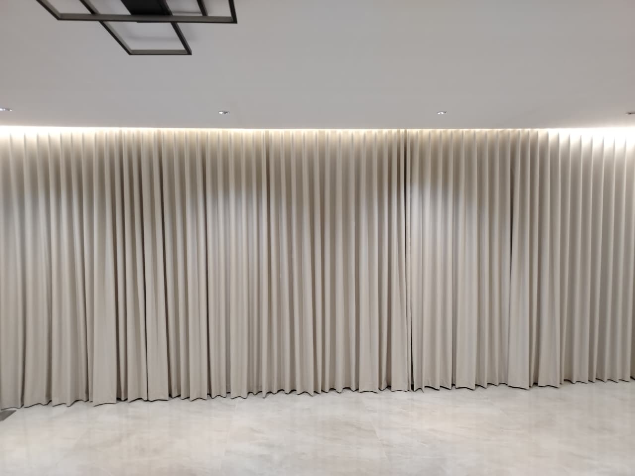 Wall-wide cream wave curtains under cove lighting